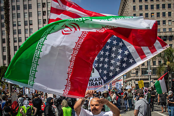 An man holds an Iranian flag and an upside down American flag while people gather for a "No War with Iran x Israel and Immigrants" on June 21, 2025...