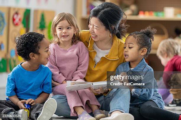 teacher reading together with excited preschool children in a classroom setting - kinderopvang stockfoto's en -beelden