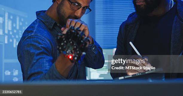 closeup black and hispanic male engineers programmers work together on robot hand prototype, use computer control robotic arm circuit in tech office night. software developer, artificial intelligence. - web prototype stock pictures, royalty-free photos & images