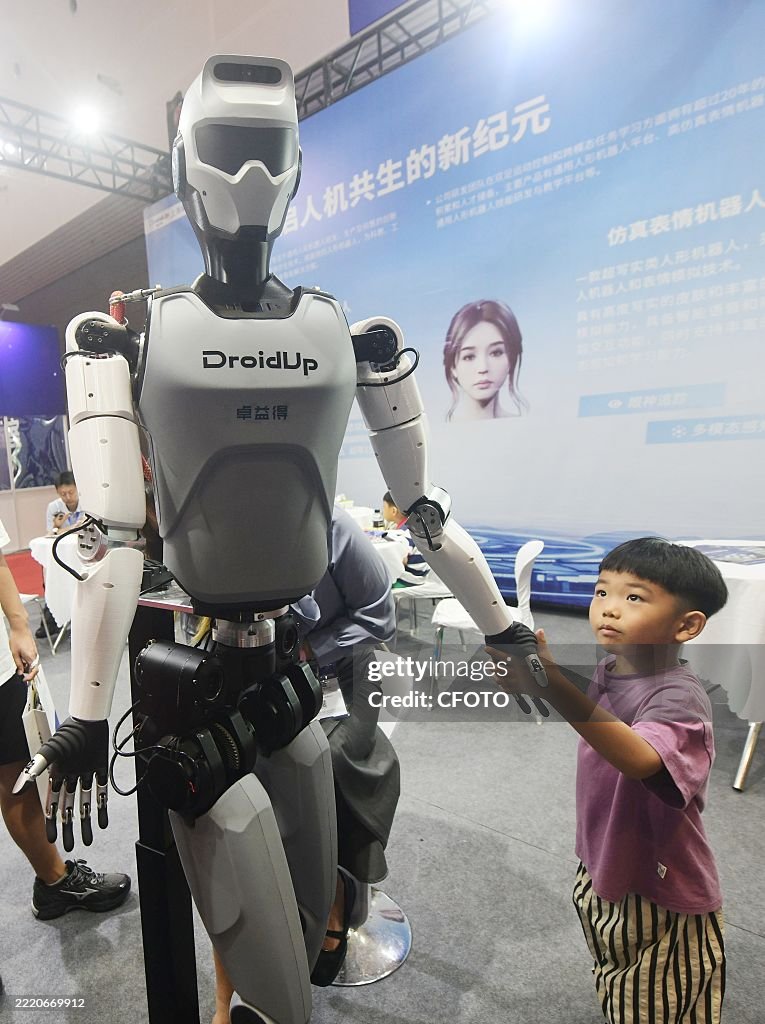 Humandroid Chaina HANGZHOU, CHINA - JUNE 22, 2025 - A young visitor touches a humanoid ...