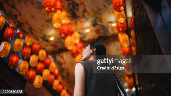 Young Asian woman looking up and admiring the illuminated traditional Chinese red lanterns hanging up in the city. Traditional Chinese cultures. Travel and vacations. Festival and celebration theme Young Asian woman looking up and admiring the illuminated traditional Chinese red lanterns hanging up in the city. Traditional Chinese cultures. Travel and vacations. Festival and celebration theme
