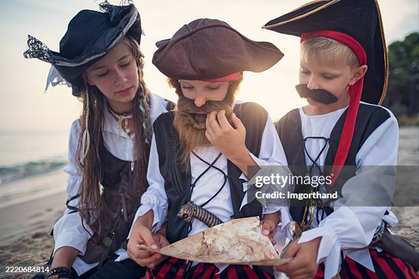kids enjoying pirate-themed beach adventure deciphering a treasure map. - schatzoeken stockfoto's en -beelden