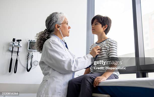 pediatrician examining a boy and listening to his heartbeat with a stethoscope - annual event stock pictures, royalty-free photos & images