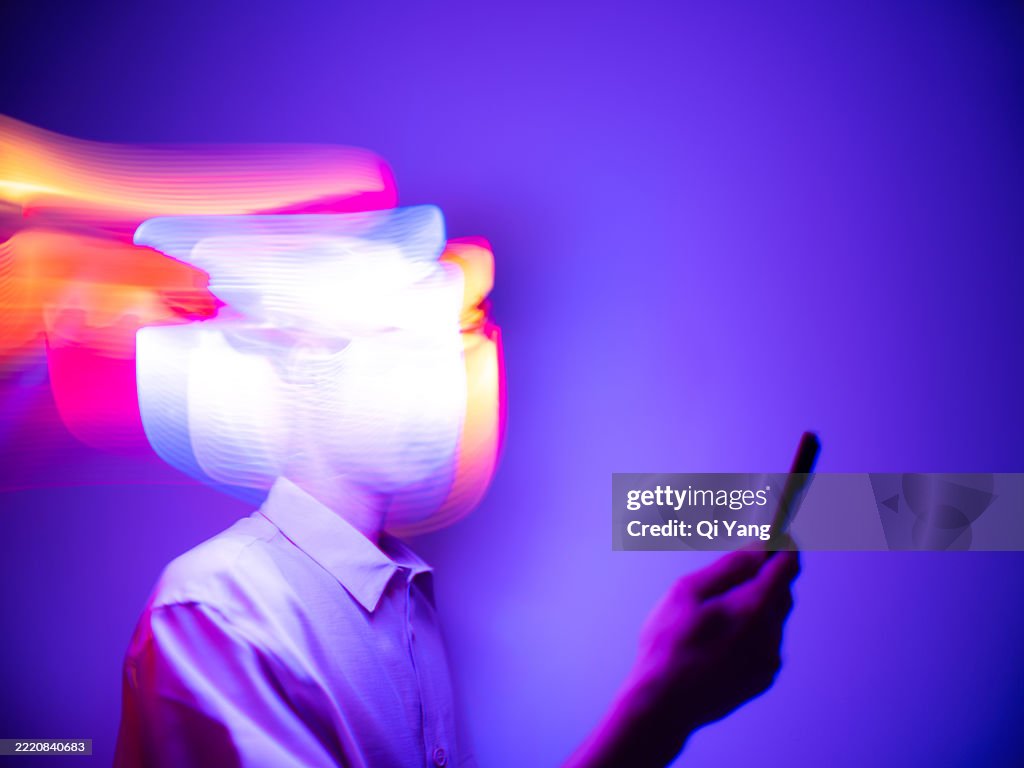 A young Asian businessman uses a smartphone while standing in a trail of flowing light. Artificial intelligence concept, Neon light long exposure