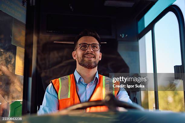 bus driver wearing safety vest smiling while driving bus - public service stock pictures, royalty-free photos & images