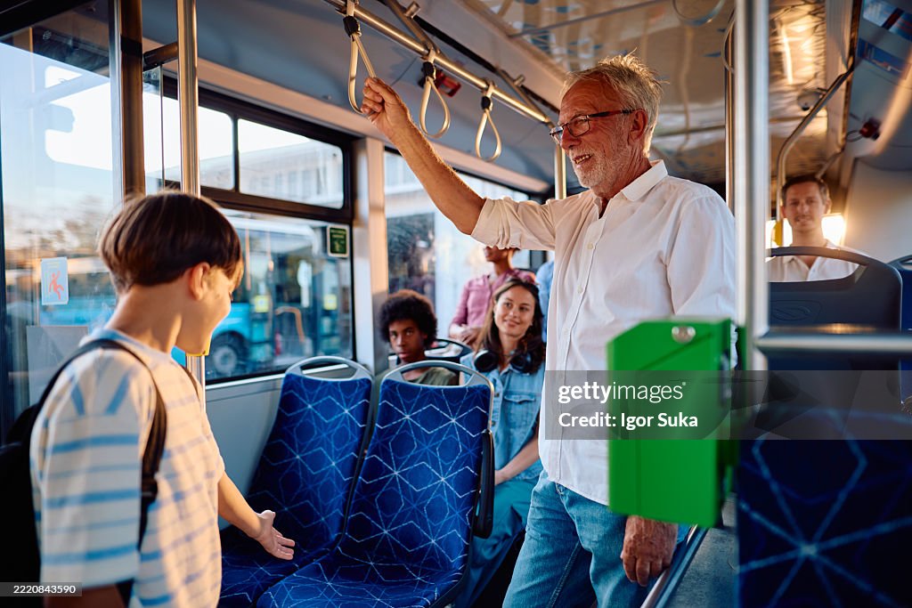 Elderly man giving up his seat on the bus to a young boy