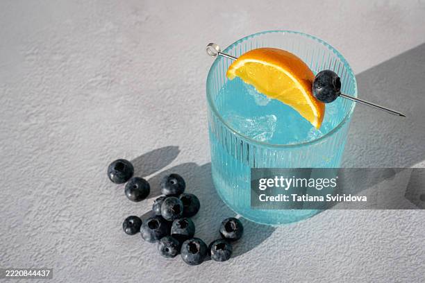 blue-colored cocktail or mocktail mocktail glass with fruit and berry garnish on a garden table - blue curacao stock pictures, royalty-free photos & images