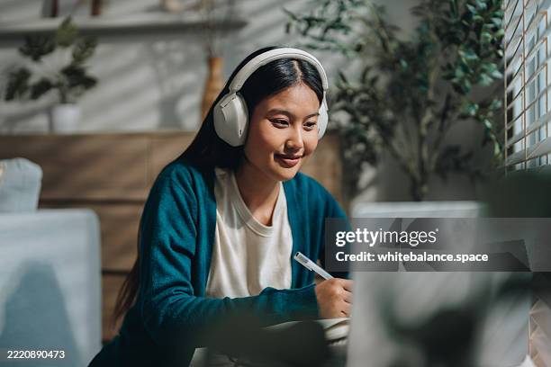 mujer disfrutando de su clase en línea, tomando notas atentamente mientras se mantiene comprometida y concentrada - educación on line fotografías e imágenes de stock