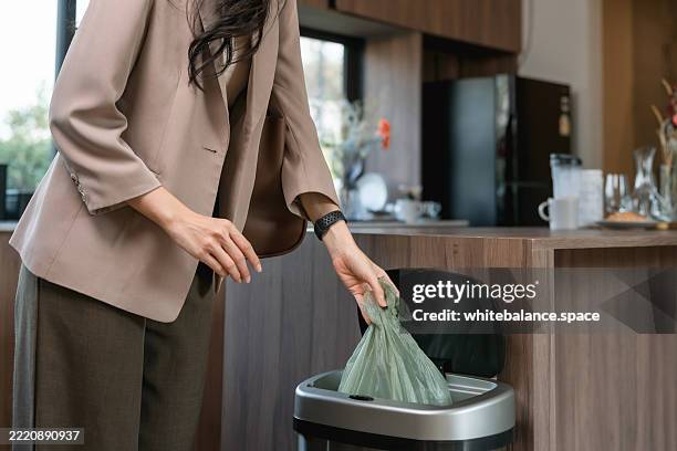 businesswoman tying up a full trash bag and putting it in the kitchen bin before heading out to work - vuilniszak stockfoto's en -beelden