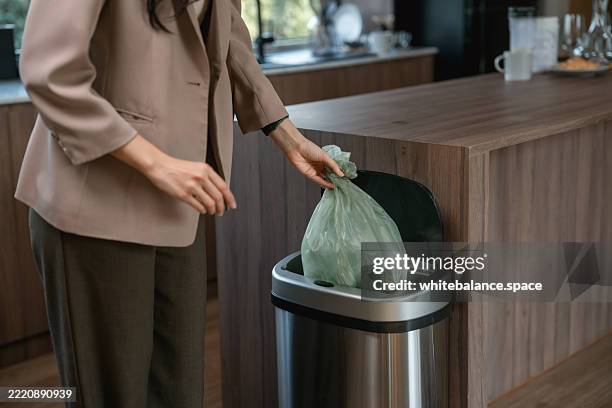 businesswoman tying up a full trash bag and putting it in the kitchen bin before heading out to work - holding garbage bag stock pictures, royalty-free photos & images