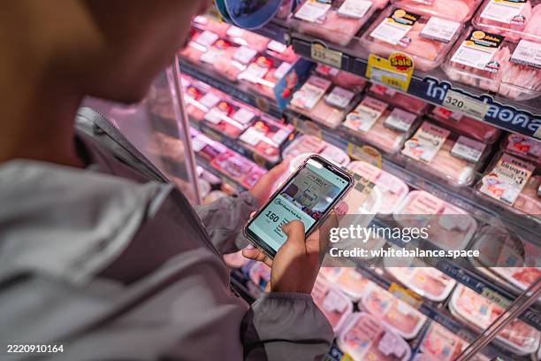 close-up shot of a man using his smartphone to check his smart fridge while grocery shopping at the supermarket - buy online pick up in store stock pictures, royalty-free photos & images