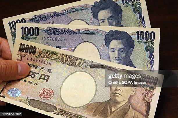 In this photo illustration, a hand holds Japanese banknotes, including 10,000 - yen and 1,000 - yen notes.