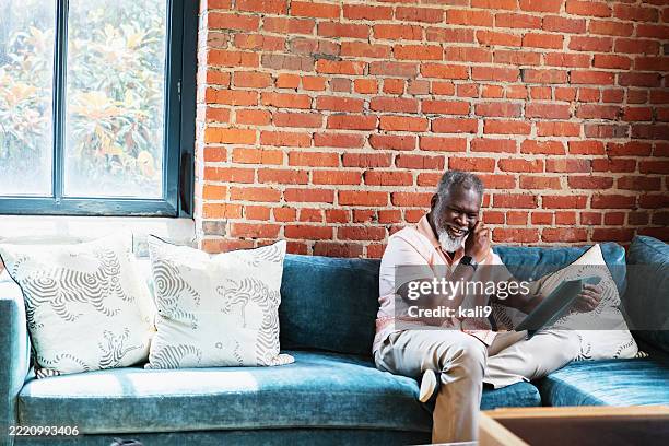 man in office lounge sitting on sofa with tablet, laughing - tears happiness stock pictures, royalty-free photos & images