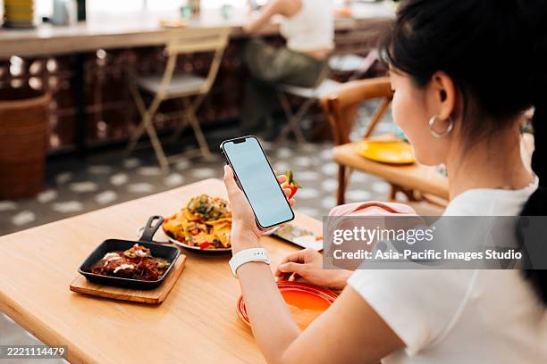 cropped shot of young asian woman using smartphone with blank white screen over dining table in restaurant. luxury lifestyle. enjoying life with good food. people, food, lifestyle and technology. - digital wallet stock pictures, royalty-free photos & images
