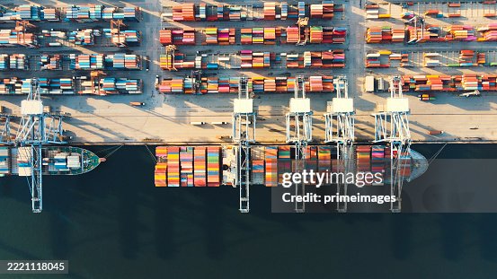 Global cargo terminal loading and unloading logistics from aerial perspective port operations with cranes and docked freight ships Global cargo terminal loading and unloading logistics from aerial perspective port operations with cranes and docked freight ships