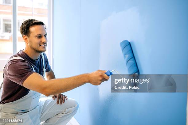 professional painter applying blue paint with roller on wall - professional painter stock pictures, royalty-free photos & images