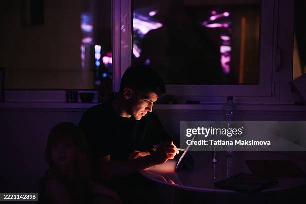 man working at a tablet in a dark room illuminated by a purple glow from the screen and window reflections. - person on computer in dark room foto e immagini stock