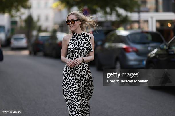 Lil Paulin is seen wearing oversized black square-framed sunglasses with orange lenses and wide temples, gold hoop earrings, a flowy sleeveless maxi...