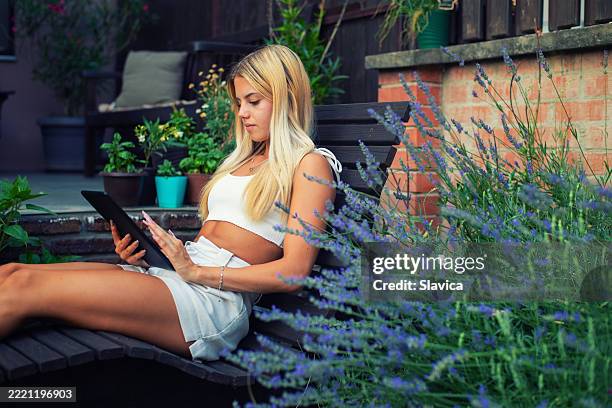 young blonde woman using digital tablet in her back yard - summer tablet stock pictures, royalty-free photos & images