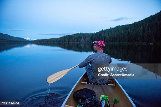 man paddles canoe on mountain lake at dusk - head torch stock pictures, royalty-free photos & images