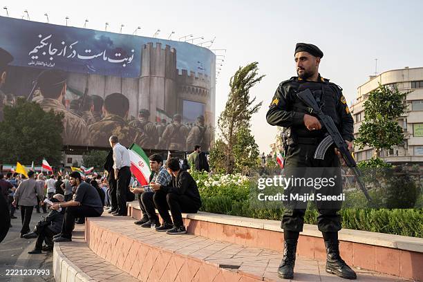 Police officer stands guard as demonstrators wave flags and cheer during a gathering to honor Iran’s military forces, following the announcement of a...