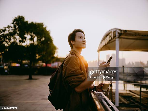young asian man using smartphone at the pier at sunset - corporate wellness program stock pictures, royalty-free photos & images