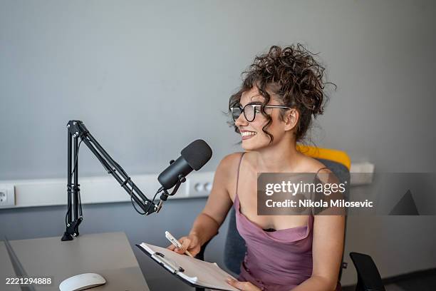 smiling woman recording content at a desk with microphone and notes - publisher stock pictures, royalty-free photos & images