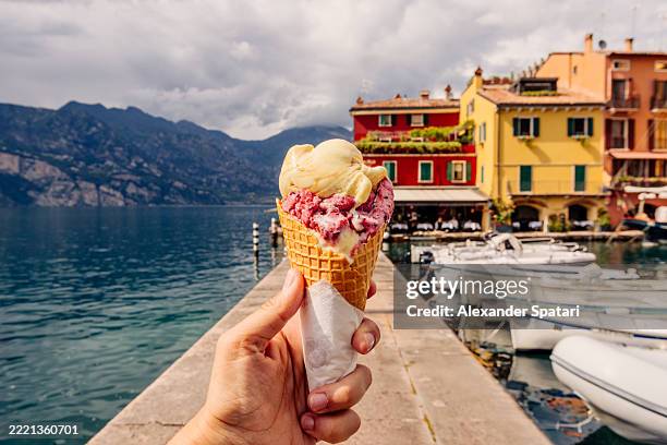 eating colourful gelato ice cream among vibrant houses in malcesine town, garda lake, italy - gelato italiano foto e immagini stock