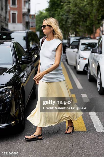 Guest wears a sleeveless white structured top with sculpted shoulders, paired with a pale yellow silk-satin A-line midi skirt, tortoiseshell cat-eye...