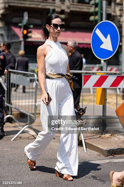 Guest wears a white halter-neck jumpsuit with a fitted bodice and wide-leg trousers. A patterned scarf in shades of gold and navy is tied around the...
