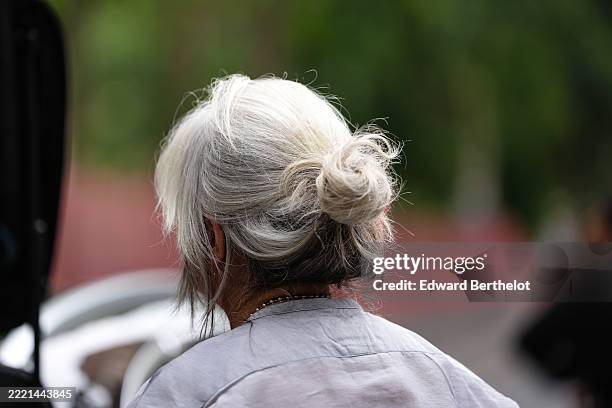 Guest wears hair styled in a loose, messy bun with a mix of white and gray tones. A light gray top is visible, featuring a simple round neckline. A...