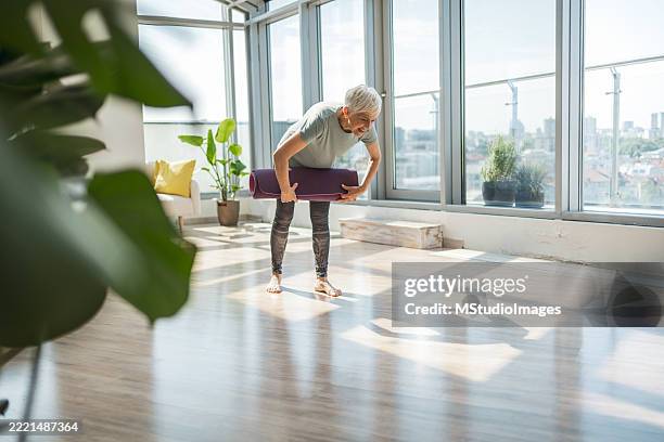 femme senior pratiquant le yoga en intérieur dans une pièce ensoleillée avec vue - chambre bien rangée photos et images de collection