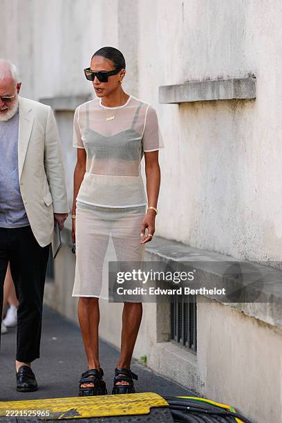 Guest wears a sheer, short-sleeved, knee-length dress in a light, translucent fabric, layered over a darker undergarment. The dress features a round...