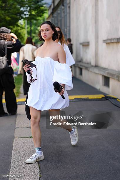 Guest wears a white, off-the-shoulder, voluminous mini dress with long, puffed sleeves. The dress appears to be made of a lightweight fabric....