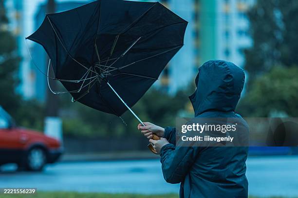 man with umbrella hiding from wind and rain. stormy weather - zwaar stockfoto's en -beelden