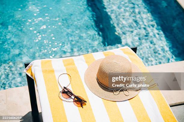 sun lounger with towel and straw hat near the pool. - silla de playa fotografías e imágenes de stock