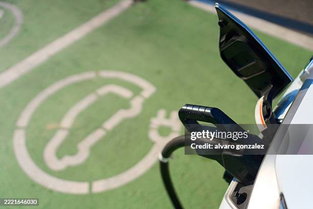 electric car plugged into charging station in parking lot - sustainability and clean energy concept - movilidad sostenible fotografías e imágenes de stock