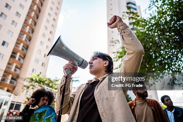 jeune homme parlant dans un mégaphone lors d’une manifestation de défenseurs de l’environnement dans une rue de la ville - justice sociale concept photos et images de collection