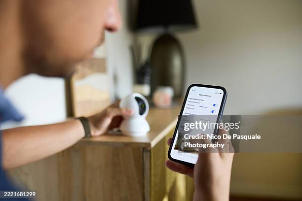 man setting up smart webcam using smartphone at home - bewakingscamera stockfoto's en -beelden
