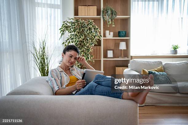 young woman relaxing on sofa using digital tablet at home - feet up stock pictures, royalty-free photos & images