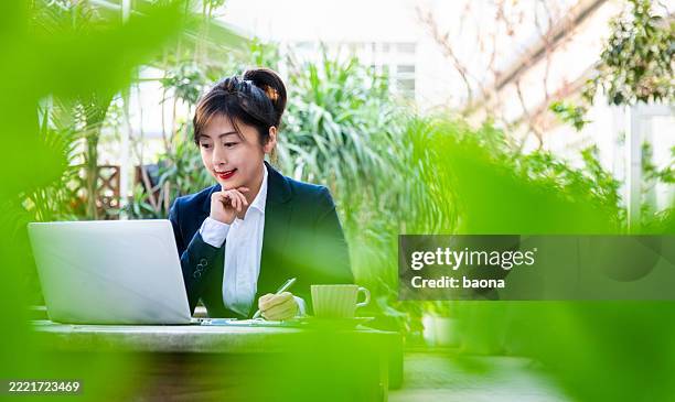 schöne geschäftsfrau, die am laptop im garten arbeitet - grüner anzug stock-fotos und bilder