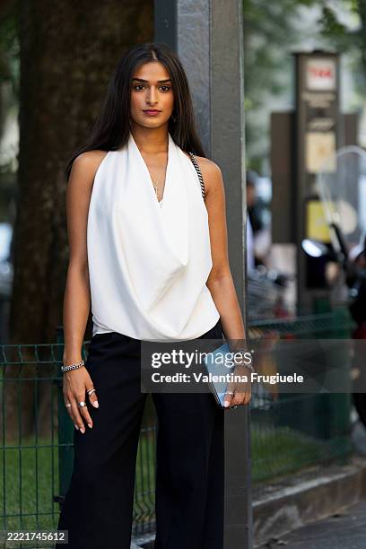Guest wears a white halter-style draped top with a plunging cowl neckline, black wide-leg tailored trousers, silver jewelry including a bracelet and...
