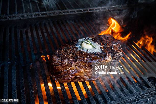 saftiges rib-eye-rindersteak, perfekt zubereitet auf einem flammenden grill mit einem klecks butter und einer prise rosmarin. eine saftige und würzige mahlzeit - rib eye steak stock-fotos und bilder