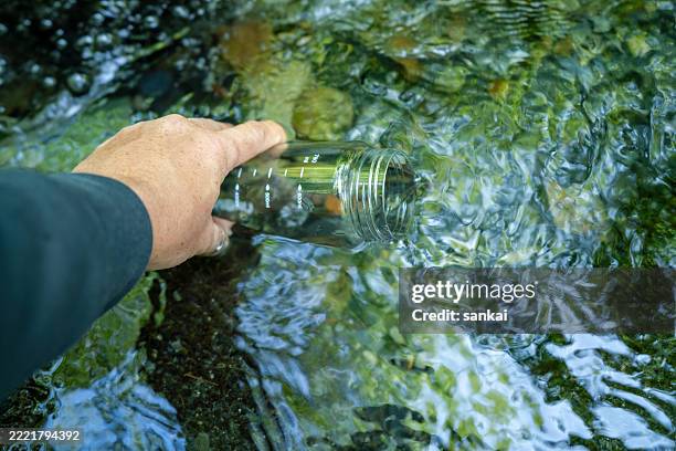 filling a transparent plastic bottle with clear stream water in a natural setting - thirsty stock pictures, royalty-free photos & images