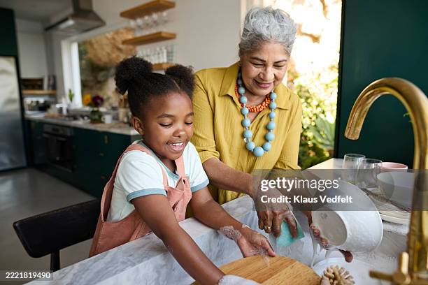 girl helping grandmother while washing dishes - chores stock pictures, royalty-free photos & images