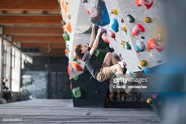 mann beim bouldern an einer indoor-kletterwand in einer modernen halle - freiklettern stock-fotos und bilder