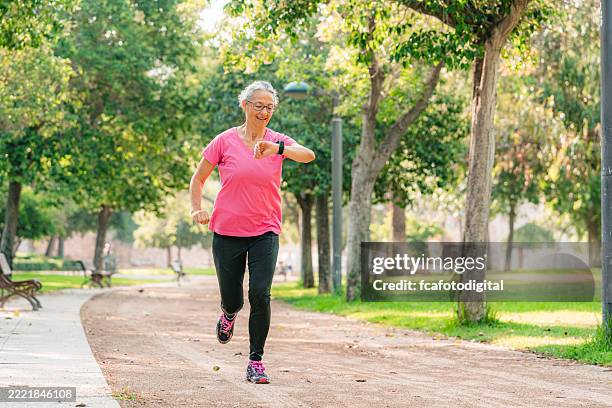 aktive senior-sportlerin, die läuft und smartwatch überprüft, trainiert für einen gesunden lebensstil und wellness in einem öffentlichen park. cardio und fitness für muskulären körperbau und herzgesundheit. - fitness tracker stock-fotos und bilder