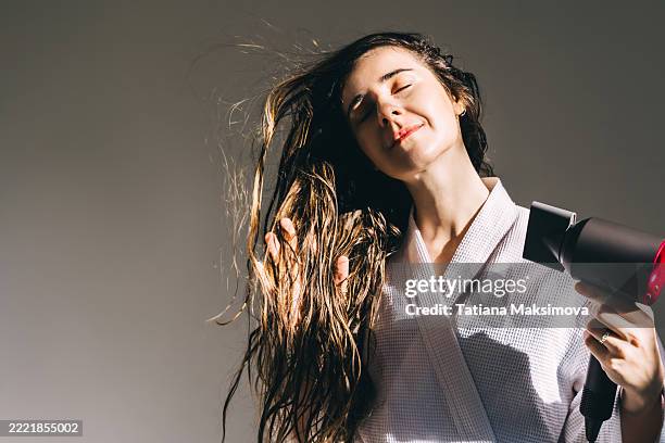 a young woman in white bathrobe blow-dries her hair at home. - menschliches haar stock-fotos und bilder