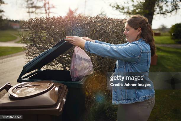 pregnant woman throwing garbage bag in trash can at back yard - garbage bag stock pictures, royalty-free photos & images