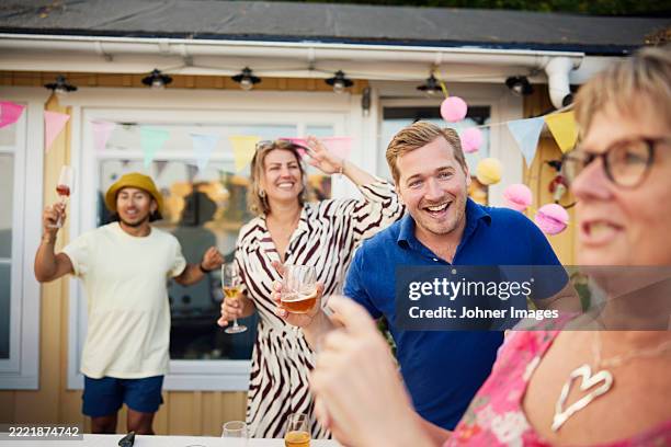 happy man holding glass of alcohol drink dancing with friends in back yard during social gathering event - neighbor stock pictures, royalty-free photos & images